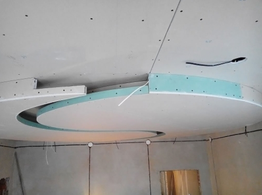 Двухъярусный потолок из гипсокартона сложной конфигурации, на фото – процесс работ по монтажу конструкции 